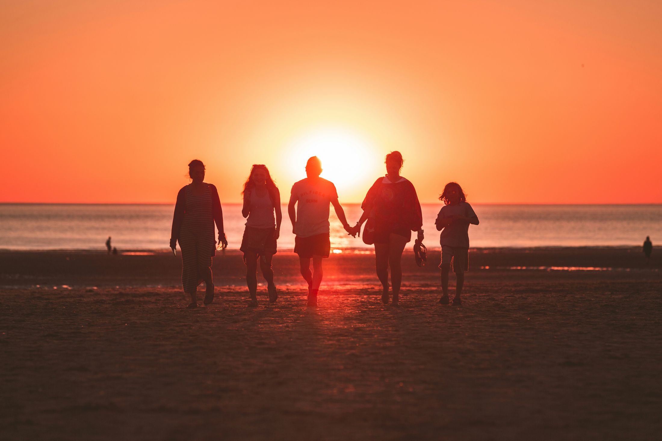 A group walking together along the shore at sunset